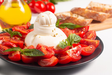 Traditional Italian burrata cheese with salad of delicious cherry tomato, basil leaves and olive oil.