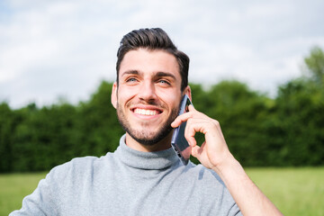 Young man with blue eyes talking on the phone outdoors in nature