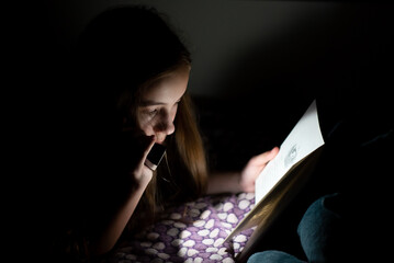 A teenage girl reads in the dark with a flashlight.