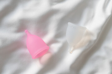 Two menstrual cups of transparent and pink color lie on a white crumpled cloth