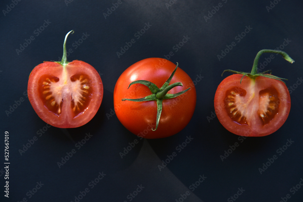 Wall mural Sliced and whole tomatoes on a black background. Juicy and delicious tomatoes close-up.