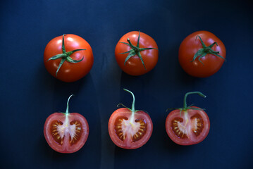 Sliced and whole tomatoes on a black background. Juicy and delicious tomatoes close-up.