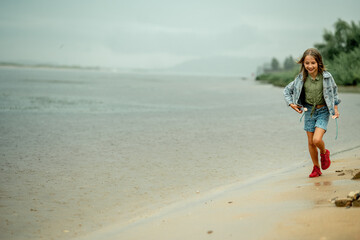 Fototapeta na wymiar A girl on a rainy day runs along the shore