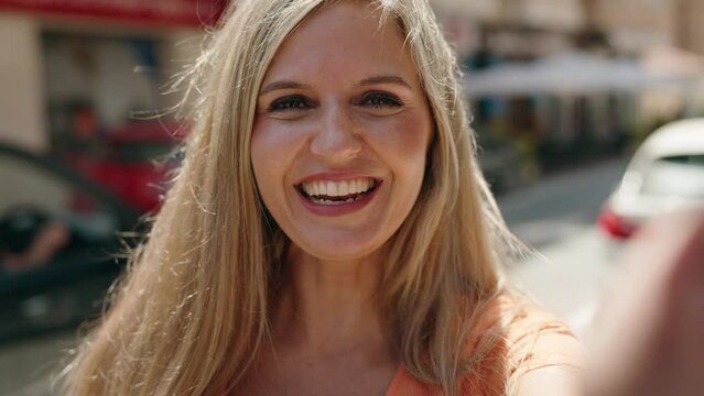 Young blonde woman smiling confident having video call at street