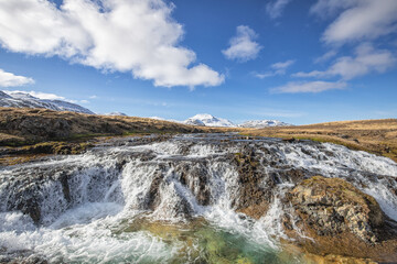 Wasserfall vor schneebedeckten Bergen und weiß blauer Himmel in Island - Snæfellsnes