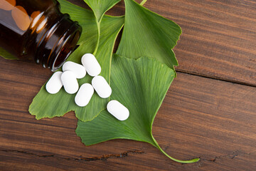 Bottle of pills and fresh ginkgo biloba leaves on wooden background. Traditional, herbal medicine...