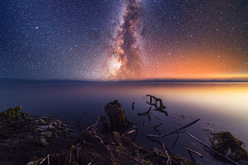 Night landscape. Beautiful lake in the night under starry sky with bright miky way galaxy. The old stump on the shore.