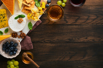 Assortment of cheese, honey, cracker, blueberries, grapes with red and white wine in glasses antipasto server on white marble board on old rustic wooden table background. Flat lay, copy space.