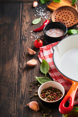 Frying pan white, black empty plate, basil leaves and spices on old wooden background. Abstract food background. Top view of dark rustic kitchen table with wooden cooking utensils, frame. Mock up.
