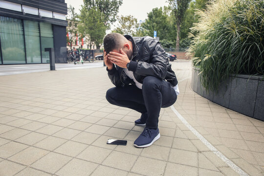 Broken glass screen of a smartphone in the hand of an upset guy on the street, a frustrated guy is sitting on the street near his broken phone