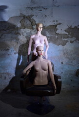 a photograph depicting a female mannequin against the background of a dirty, damp wall of an old room.