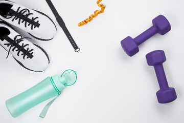 Sports composition with dumbbells, measuring tape, sneakers, water bottle and electronic bracelet on a white background. Gym stuff, sports equipment, copy space. Flat lay composition.