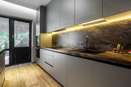Modern luxury apartment with a free layout in a loft style in gray and dark colors. Stylish kitchen area with an island, marble countertop