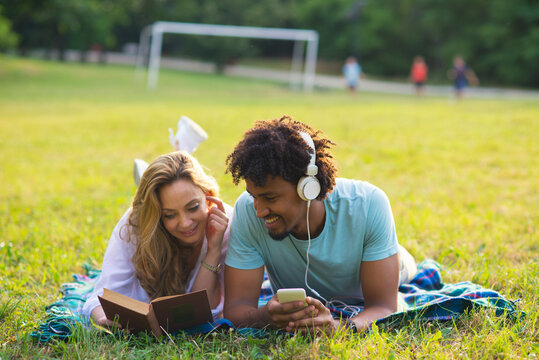 Young smiling couple lying on the meadow grass on a sunny summer day - Powered by Adobe