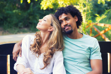 Young mixed race couple talking while sitting on the bench in the summer nature