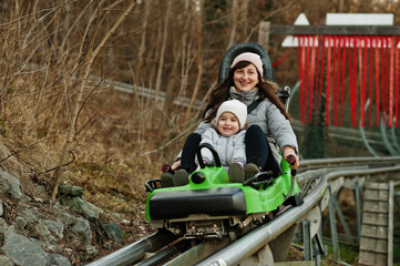Mother with daughter ride electric sleigh on rails. - obrazy, fototapety, plakaty