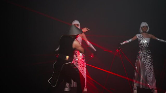 Man in samurai costume with laser light dancing with women in cyber dresses standing at black background. Front view portrait of professional Caucasian performers on stage