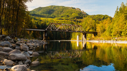 Skykomish River reflecting the railway bridge as the trees begin to turn fall colors in Western Washington State