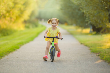 Happy beautiful little girl fast running and riding on first bike without pedals on sidewalk at...