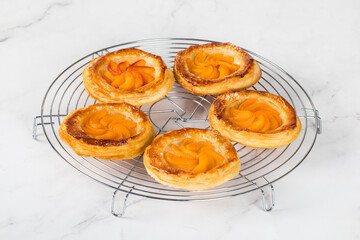 Mini open pies made of puff pastry with a filling of apricots, on a serving metal stand. Light background