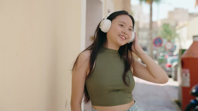 Young chinese woman listening to music and dancing at street