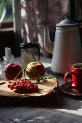 Still life in old rustic kitchen with red apples and a bunch of red rowan lying on old book, autumn morning tea concept.