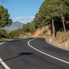 Empty winding paved road along picturesque red clay cliff partially overgrown with trees and bushes with blue sky and white clouds in background. Sunny summer day.	S shape road