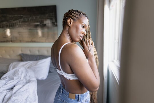 Beautiful woman in bra with long blonde braids at bedroom window