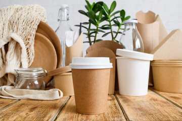 Close-up of a paper disposable cup against the background of a set of eco-friendly tableware and a green plant. Zero waste concept. Selective focus on cup