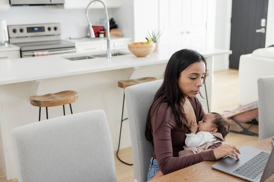 Mother breastfeeding baby daughter and working from home at laptop