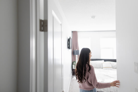 Young brunette woman with long hair standing in bedroom doorway