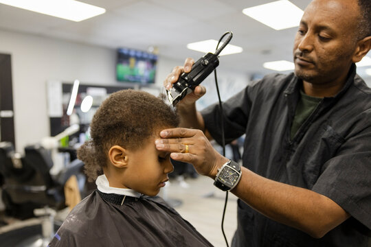 Barber with electric razor cutting hair of boy in barber shop