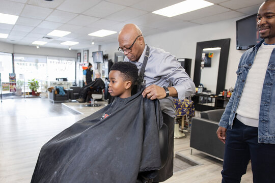 Barber putting cape on boy customer in barber shop chair