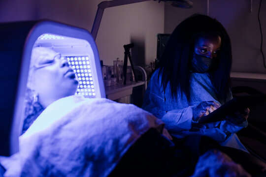 Esthetician sitting next to customer receiving blue light therapy