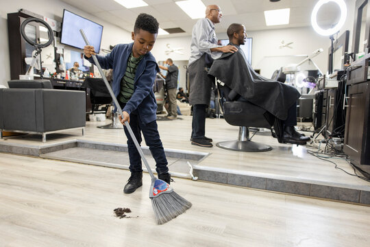 Boy with broom sweeping hair on barber shop floor