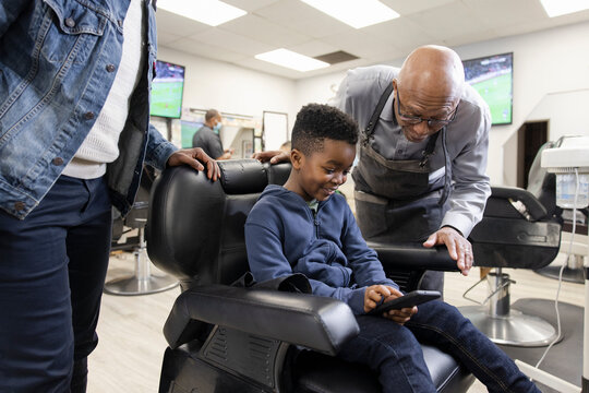 Boy customer showing smart phone to barber in barber shop chair