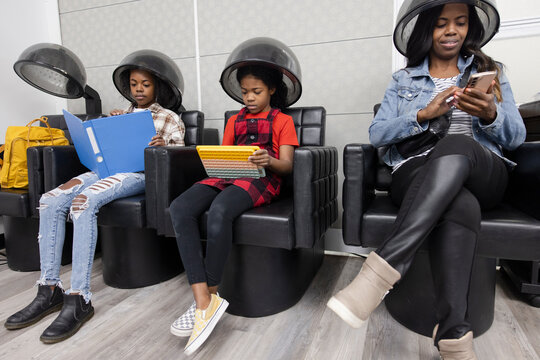 Mother and daughters under hairdryers, reading in hair salon