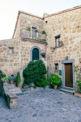 Fototapeta na wymiar Exterior shot of spectacular ancient buildings of stones with cobblestone courtyard in the foreground and with stone stairway to entrance door decorated with plants in flower pots and climbing plants,