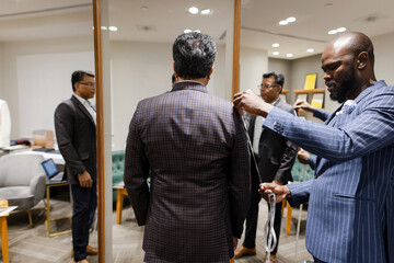 Male tailor measuring customer for suit at mirror in menswear shop