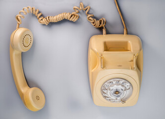 Old yellow antique rotary telephone with removed receiver on blue background. Vintage landline home phone with dial, twisted cable and reciever handset. Conversation apparatus. Top view. - obrazy, fototapety, plakaty
