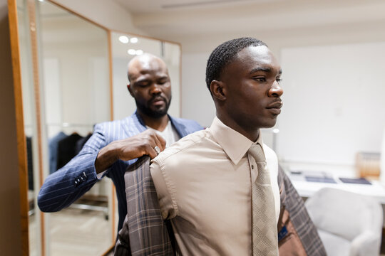 Tailor helping customer trying on suit in menswear shop