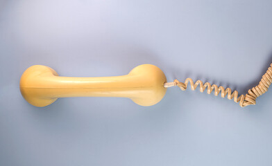 Yellow telephone receiver with twisted cord from an old antique rotary phone on blue background. Plastic removed handset from retro phone with cable. Concept of communication. Top view.