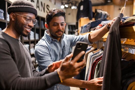 Men with smart phone shopping for shirt in clothing store