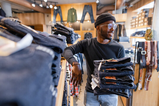 Smiling male worker with stack of jeans working in clothing store