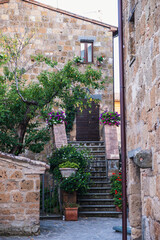 Exterior shot of spectacular ancient buildings of stones with cobblestone courtyard in the foreground and with stone stairway to entrance door decorated with plants in flower pots and climbing plants,