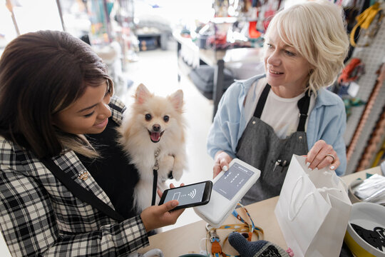 Woman with cute dog paying pet store owner with smart phone