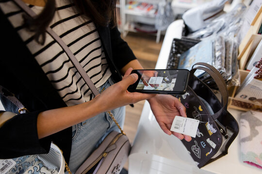 Young woman photographing price tag on handbag in shop