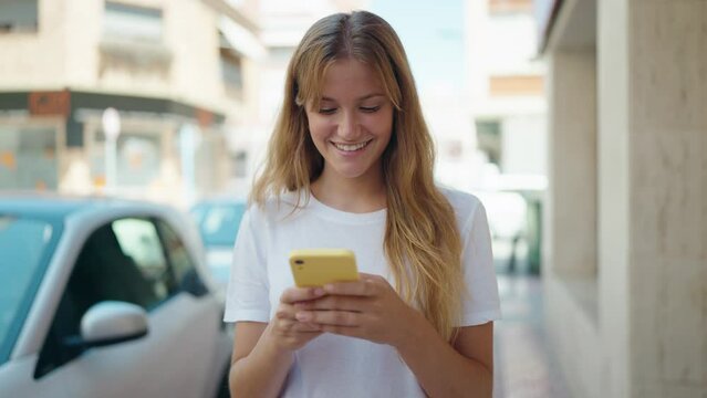 Young blonde girl smiling confident using smartphone at street