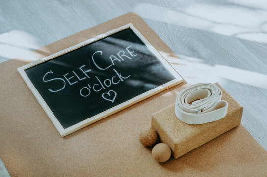 Chalkboard with Self Care o'clock message reminder on cork yoga mat with props