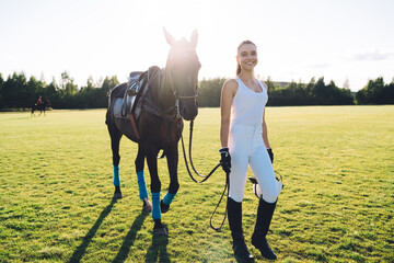 Cheerful horsewoman walking on field with horse